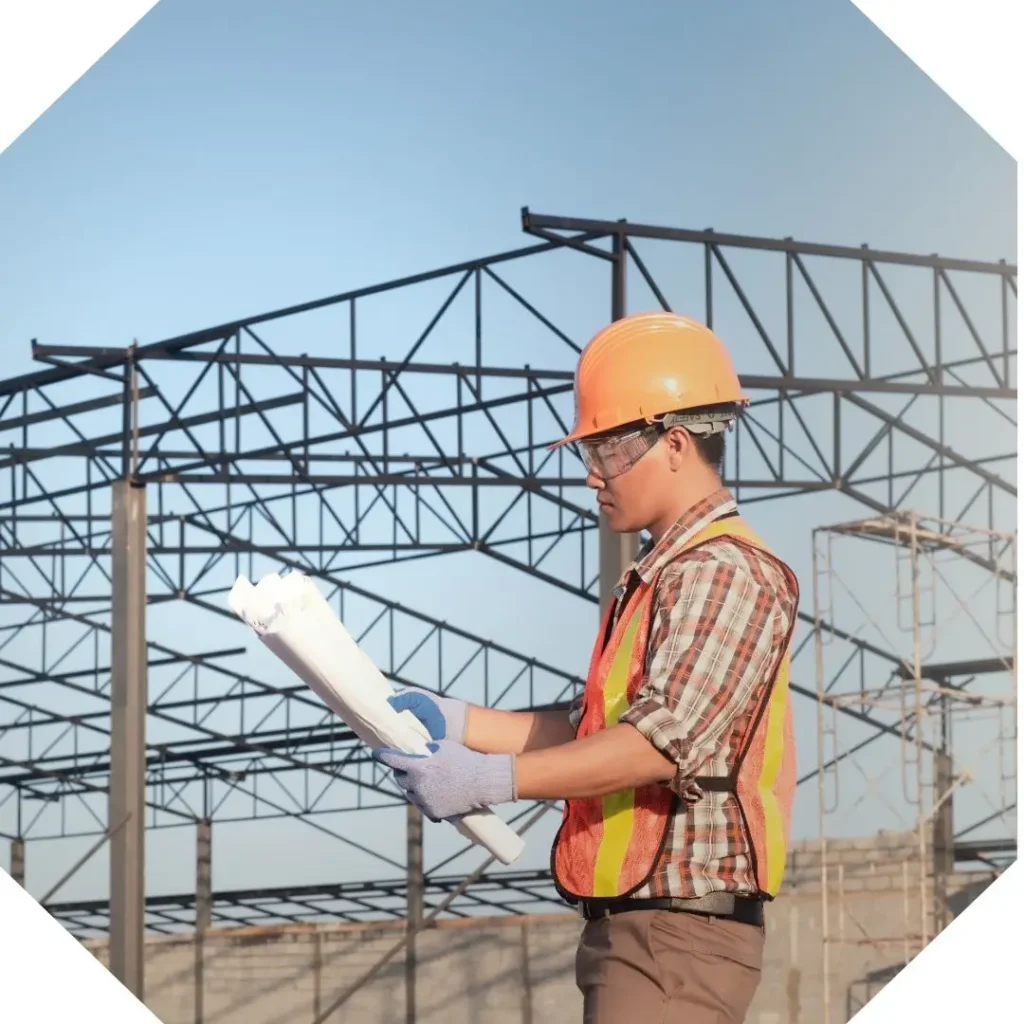 profissional eletricista analisando projeto com um galpão industrial em construção nos fundos.